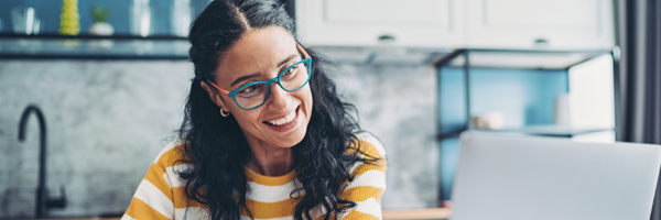 woman smiling as she works at a laptop from her kitchen table